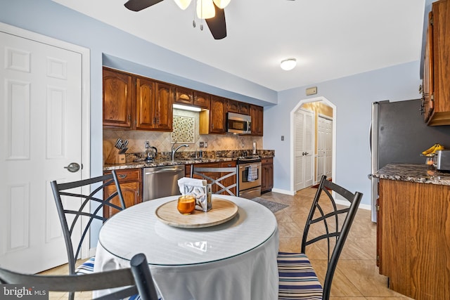 kitchen featuring light tile patterned floors, stainless steel appliances, a sink, baseboards, and decorative backsplash