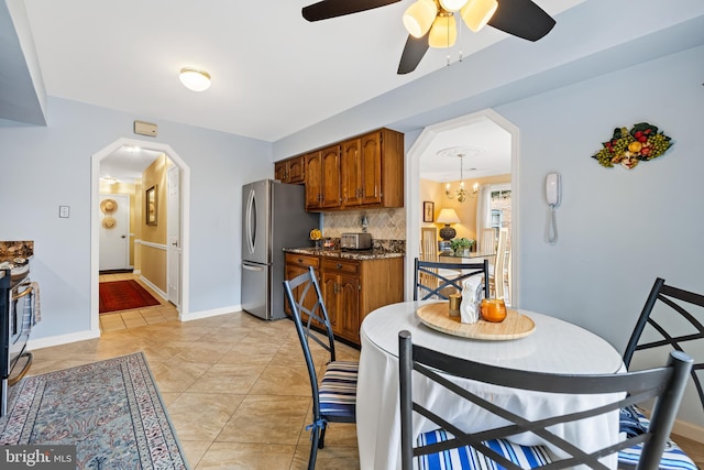 kitchen featuring baseboards, arched walkways, decorative backsplash, appliances with stainless steel finishes, and brown cabinets