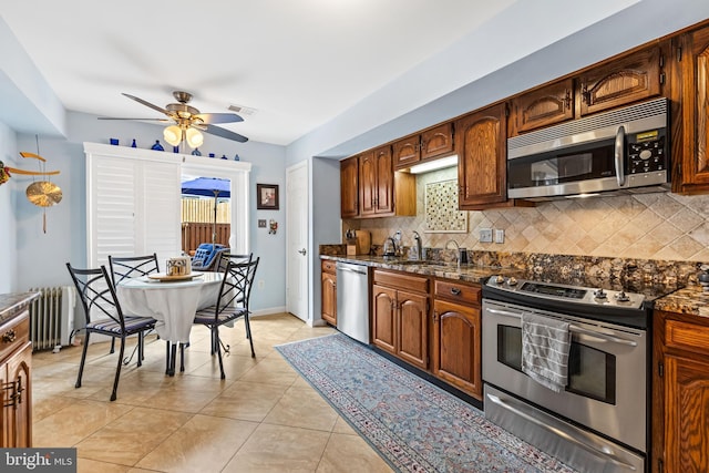 kitchen featuring radiator heating unit, stainless steel appliances, decorative backsplash, and light tile patterned flooring