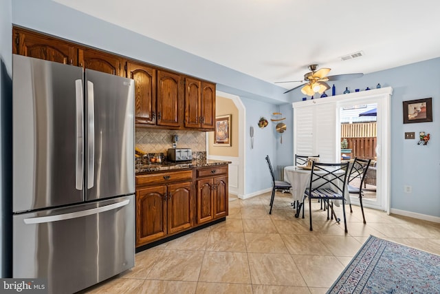 kitchen with visible vents, arched walkways, a ceiling fan, freestanding refrigerator, and backsplash