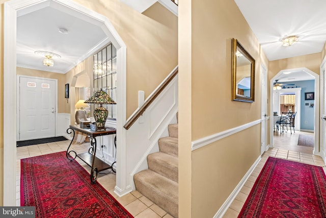 tiled entrance foyer featuring stairs, arched walkways, a ceiling fan, and ornamental molding