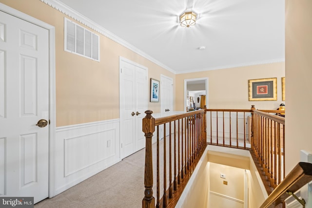 corridor with visible vents, a wainscoted wall, ornamental molding, carpet, and an upstairs landing