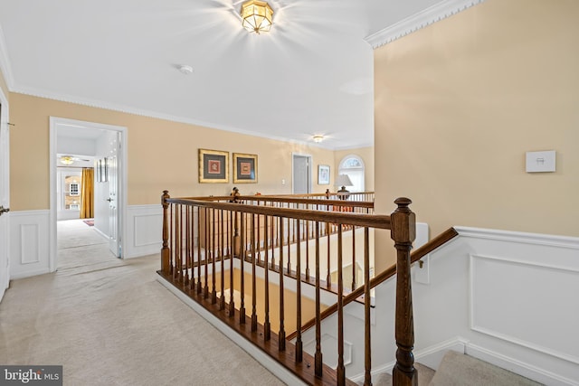 hallway with light colored carpet, a wainscoted wall, crown molding, an upstairs landing, and a decorative wall