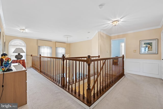 hallway featuring light colored carpet, a wainscoted wall, ornamental molding, an upstairs landing, and a decorative wall