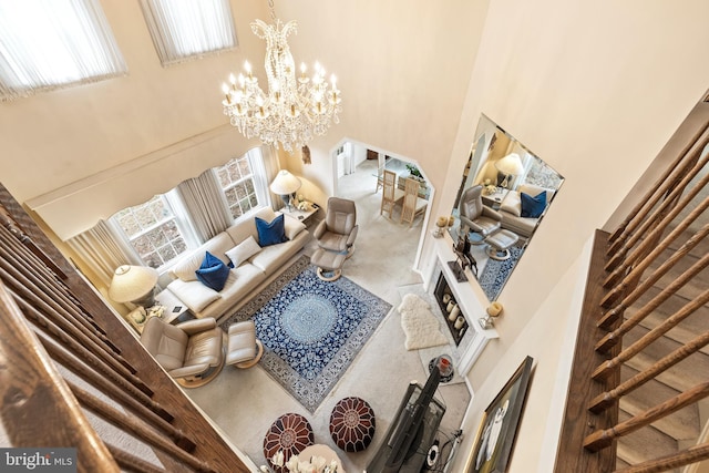 carpeted living area with arched walkways, a towering ceiling, and a notable chandelier