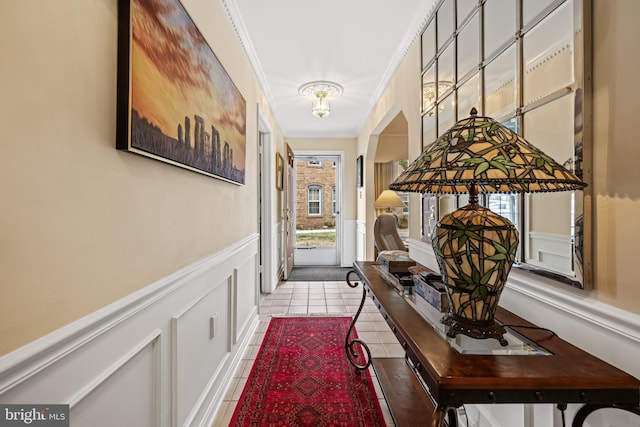 doorway to outside featuring tile patterned flooring, ornamental molding, a decorative wall, and wainscoting