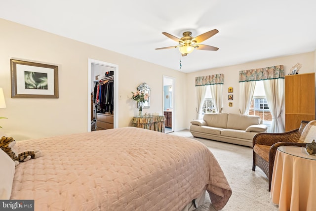 bedroom featuring light carpet, a ceiling fan, a closet, a walk in closet, and ensuite bath