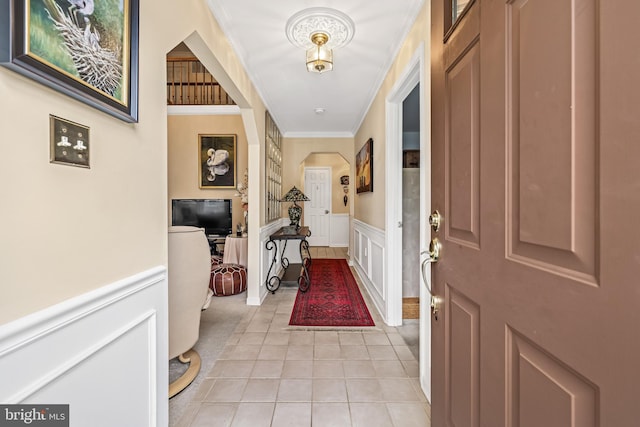 foyer featuring light tile patterned floors, arched walkways, a wainscoted wall, ornamental molding, and a decorative wall