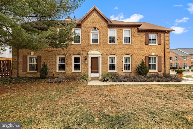 view of front facade with a front yard, brick siding, and a chimney