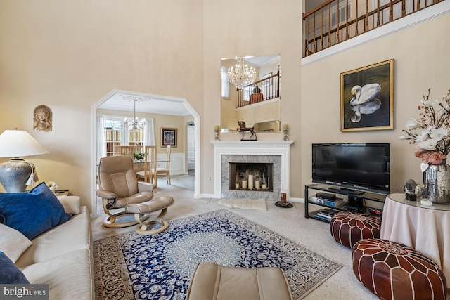 living area featuring arched walkways, a notable chandelier, a fireplace, carpet flooring, and a towering ceiling