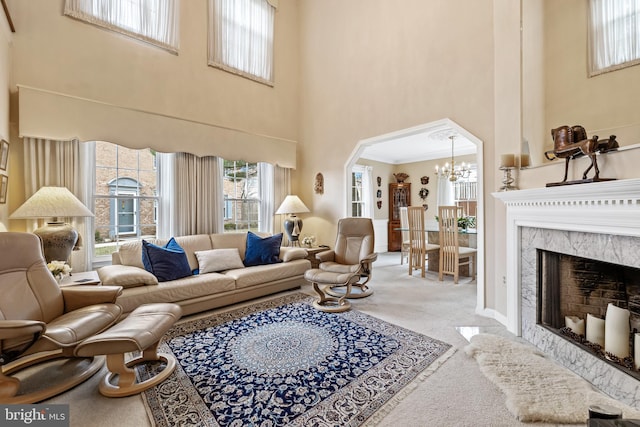 living area with arched walkways, a towering ceiling, a premium fireplace, carpet floors, and a notable chandelier