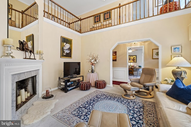 living area with arched walkways, a high ceiling, carpet flooring, and a high end fireplace