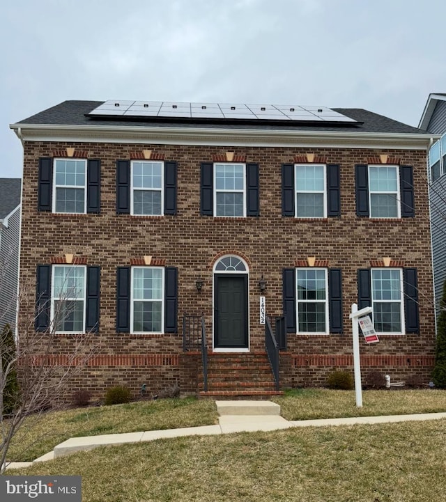 view of front of home with roof mounted solar panels, a front lawn, and brick siding