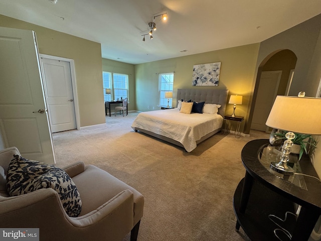 bedroom with track lighting, arched walkways, carpet flooring, and baseboards