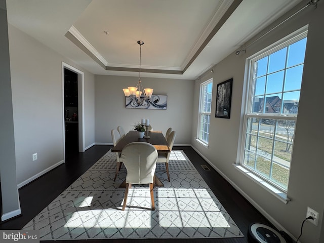 dining space with dark wood-type flooring, baseboards, an inviting chandelier, a raised ceiling, and crown molding