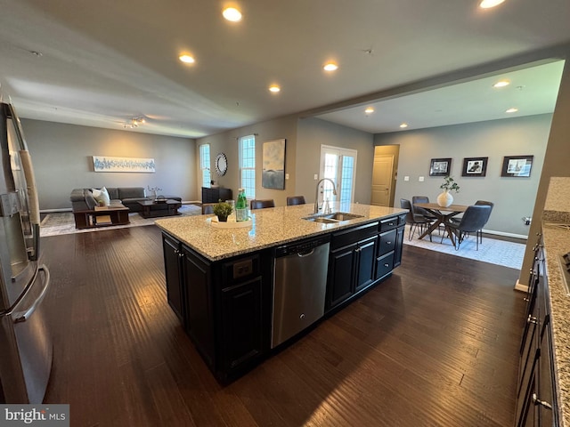 kitchen featuring open floor plan, dark wood-style flooring, stainless steel appliances, dark cabinetry, and a sink