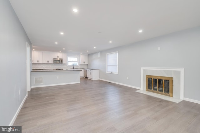 unfurnished living room with visible vents, baseboards, light wood-style flooring, a premium fireplace, and recessed lighting