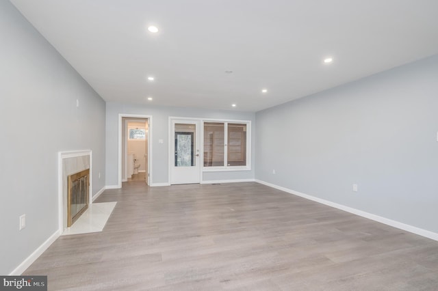 unfurnished living room featuring baseboards, light wood finished floors, a fireplace, and recessed lighting