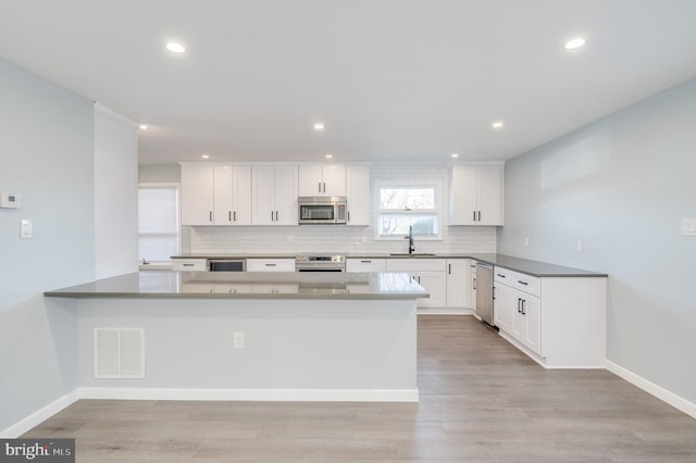 kitchen with a peninsula, a sink, visible vents, appliances with stainless steel finishes, and backsplash