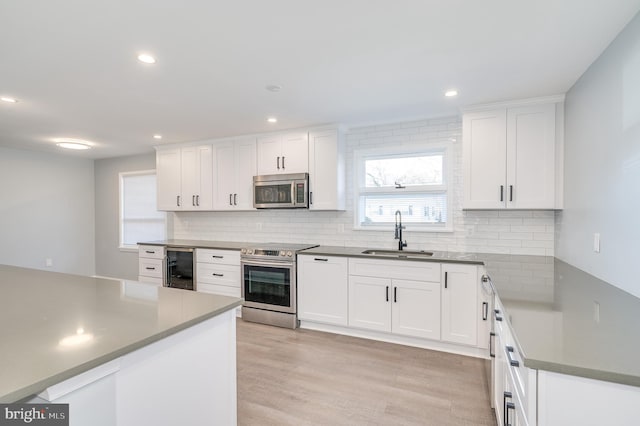 kitchen with decorative backsplash, appliances with stainless steel finishes, white cabinetry, a sink, and beverage cooler