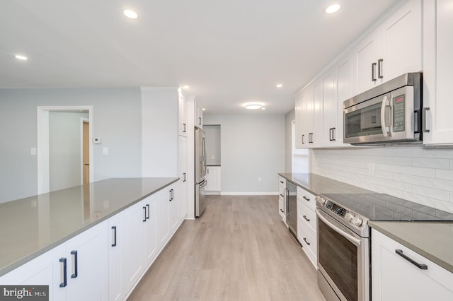 kitchen with appliances with stainless steel finishes, light wood-type flooring, white cabinetry, and decorative backsplash