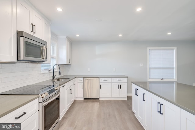 kitchen featuring stainless steel appliances, backsplash, light wood-style flooring, white cabinetry, and a sink