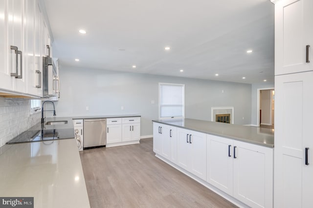 kitchen with light wood finished floors, backsplash, appliances with stainless steel finishes, white cabinets, and a sink