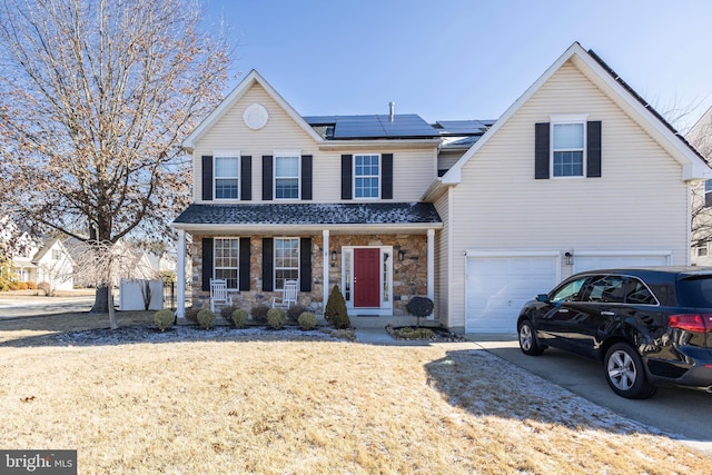 traditional home featuring solar panels, concrete driveway, covered porch, a garage, and stone siding