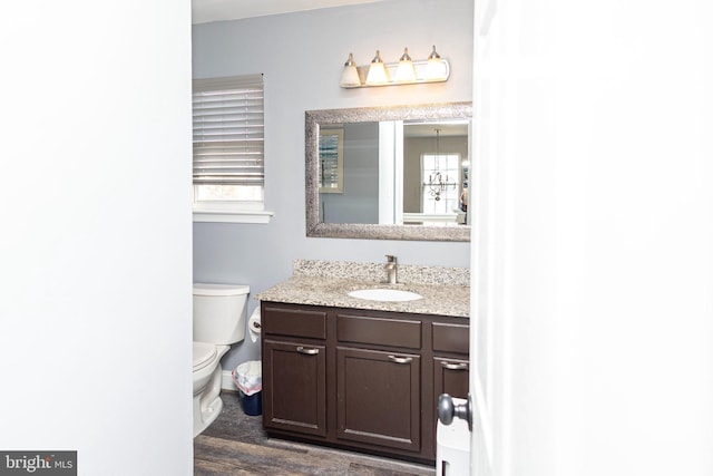 half bathroom with toilet, wood finished floors, a wealth of natural light, and vanity