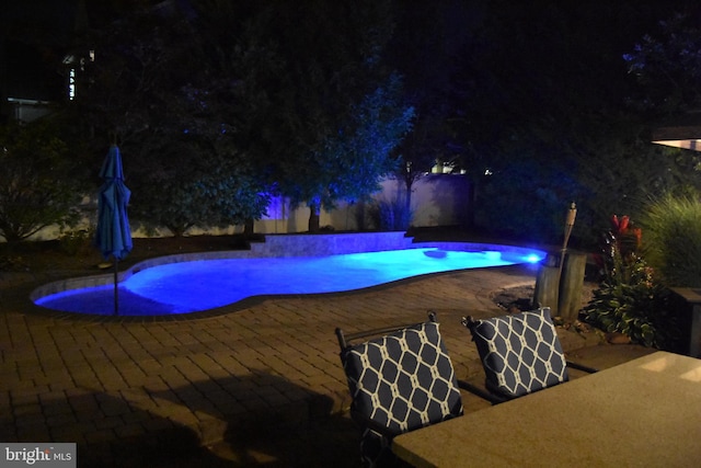 pool at night with a fenced in pool and a patio