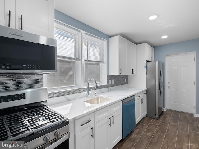 kitchen featuring tasteful backsplash, white cabinets, appliances with stainless steel finishes, light stone countertops, and a sink