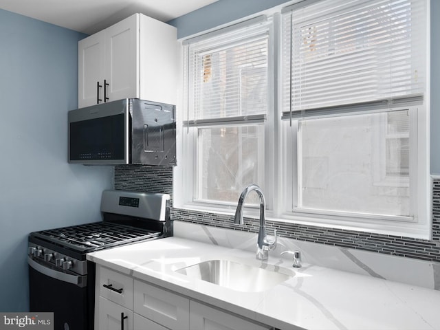 kitchen with stainless steel gas range oven, a sink, white cabinetry, light stone countertops, and tasteful backsplash