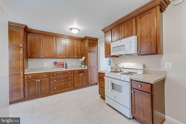 kitchen with brown cabinets, white appliances, baseboards, and light countertops