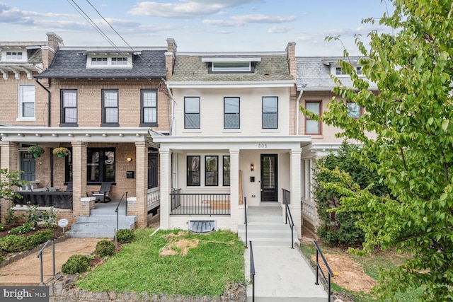 townhome / multi-family property with covered porch, a high end roof, mansard roof, and brick siding