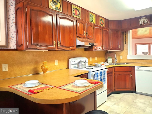 kitchen featuring white appliances, a peninsula, light countertops, under cabinet range hood, and a sink