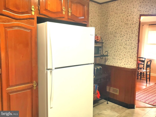 kitchen with a wainscoted wall, brown cabinetry, freestanding refrigerator, and wallpapered walls