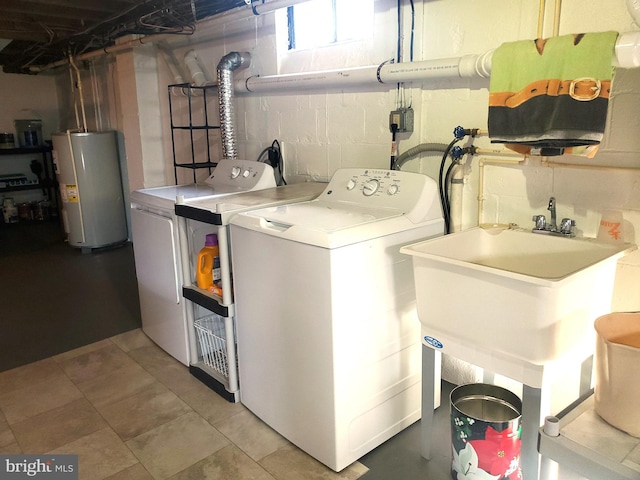 clothes washing area featuring concrete block wall, laundry area, washing machine and dryer, and water heater