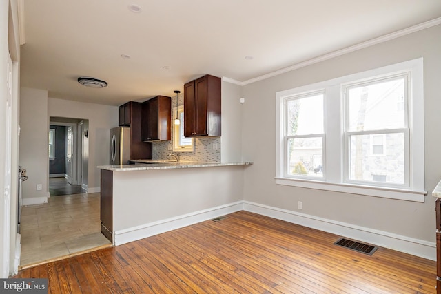 kitchen with light wood finished floors, visible vents, decorative backsplash, freestanding refrigerator, and baseboards