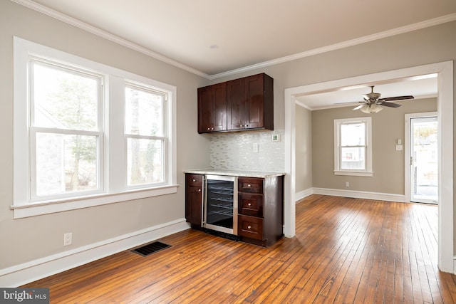 kitchen featuring tasteful backsplash, visible vents, hardwood / wood-style flooring, wine cooler, and crown molding