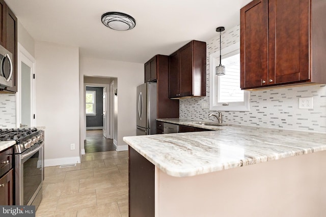 kitchen with a peninsula, a sink, baseboards, appliances with stainless steel finishes, and pendant lighting