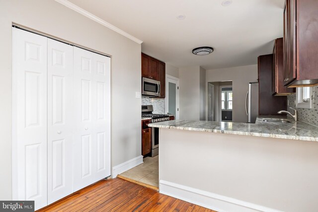 kitchen with stainless steel appliances, backsplash, a sink, light wood-type flooring, and a peninsula