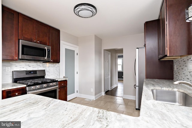 kitchen with light tile patterned floors, tasteful backsplash, baseboards, stainless steel appliances, and a sink