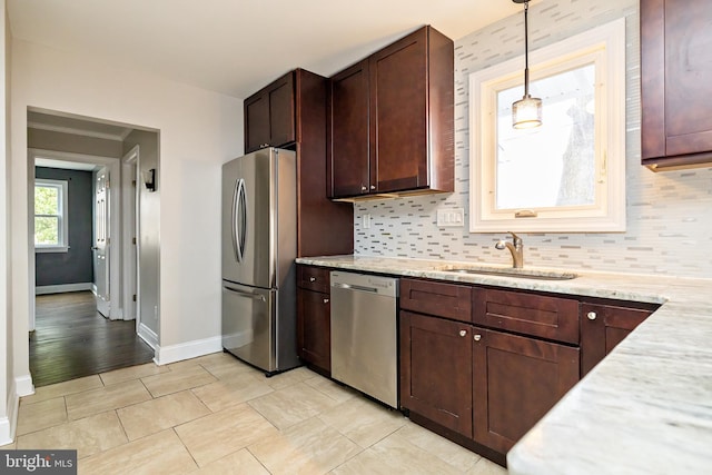 kitchen with light stone counters, stainless steel appliances, a sink, backsplash, and decorative light fixtures