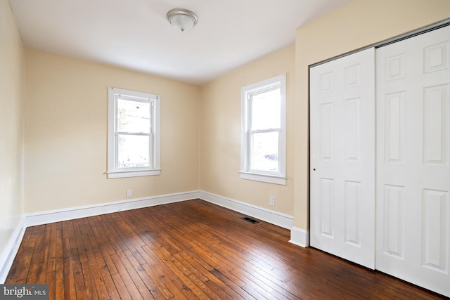 unfurnished bedroom with dark wood-style floors, multiple windows, and visible vents