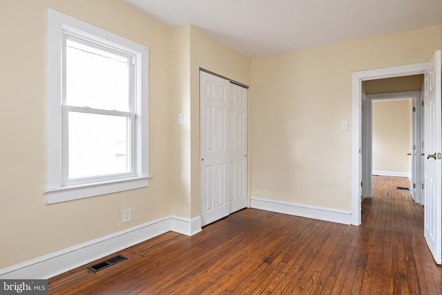 unfurnished bedroom with dark wood-style flooring, a closet, visible vents, and baseboards