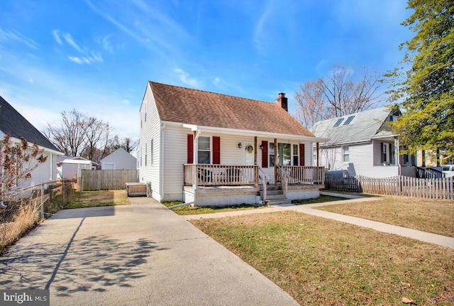 view of front facade featuring covered porch, a shingled roof, fence, a chimney, and a front yard