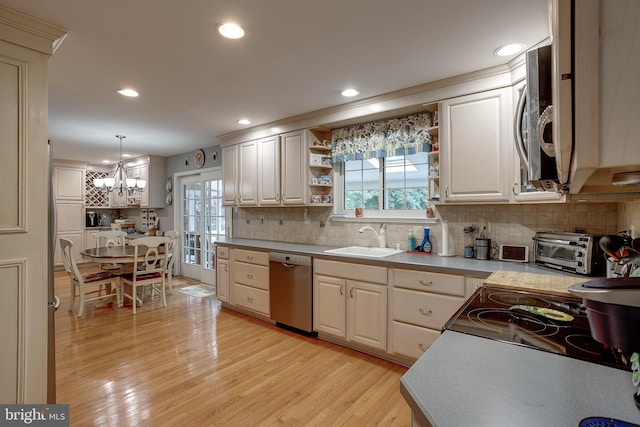 kitchen with light wood finished floors, decorative backsplash, appliances with stainless steel finishes, light countertops, and a sink