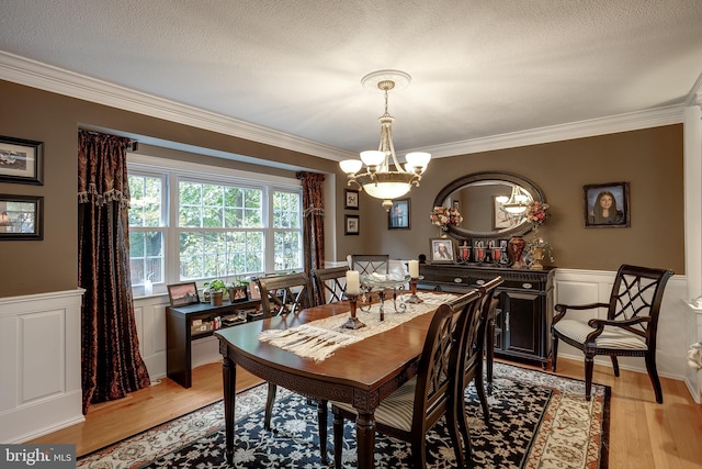 dining area with a wainscoted wall, light wood-style flooring, and crown molding