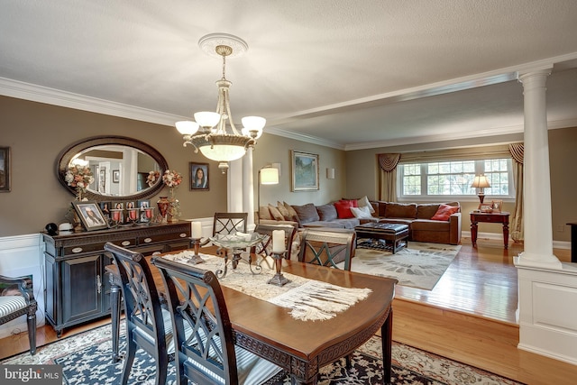 dining room with crown molding, light wood finished floors, an inviting chandelier, and ornate columns