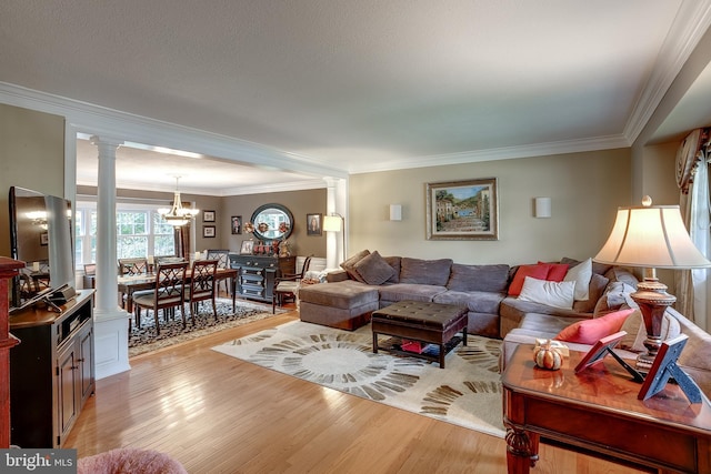 living room featuring a chandelier, light wood finished floors, decorative columns, and crown molding